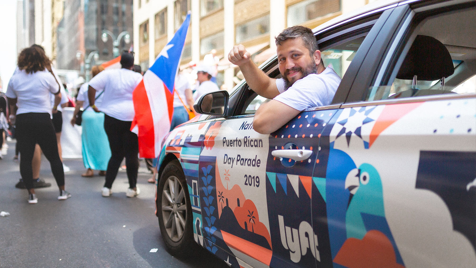 A Lyft car wrapped in National Puerto Rican Day Parade 2019 livery, a rider cheering from the window amid Puerto Rican flags